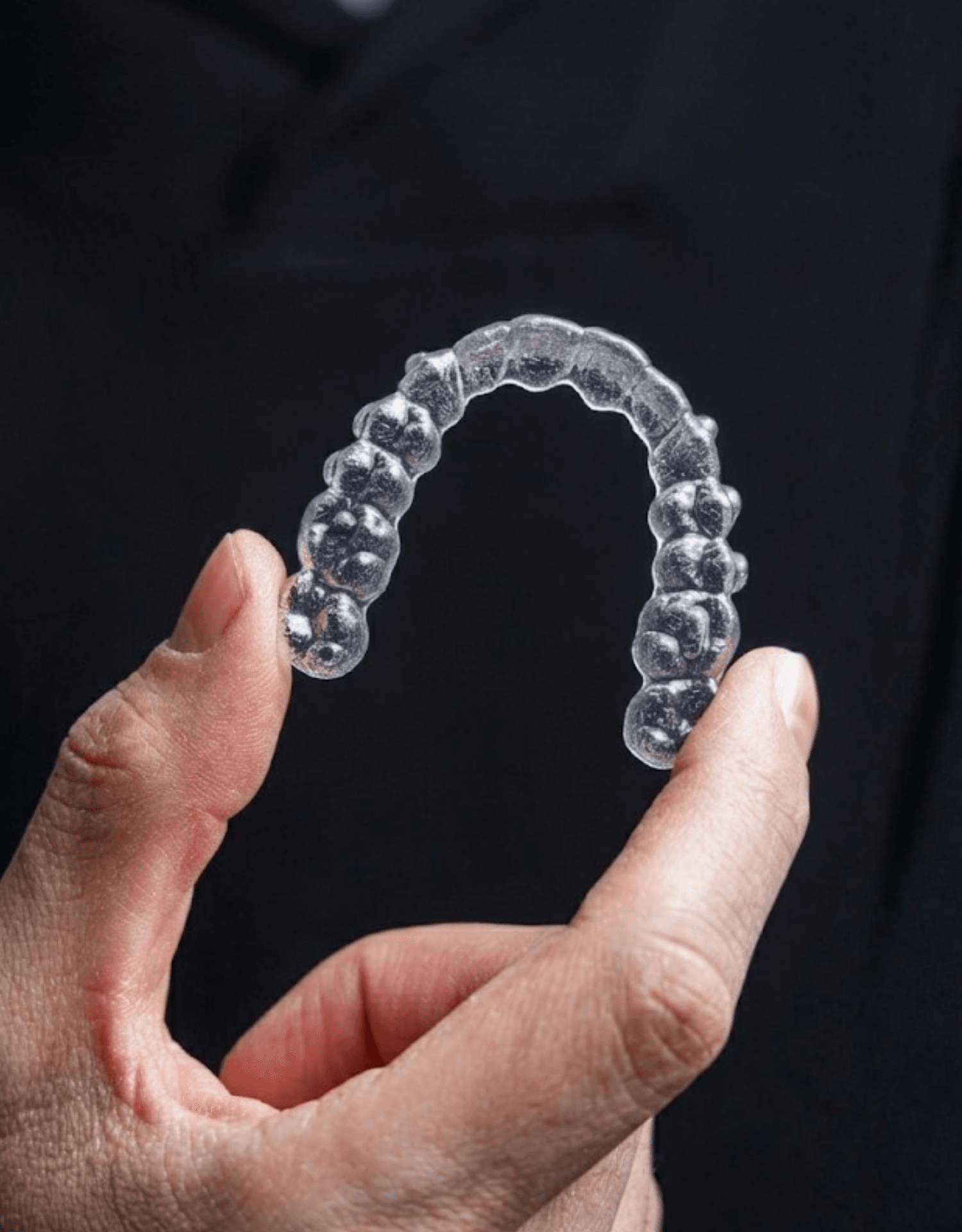 A clear aligner held up between finger and thumb